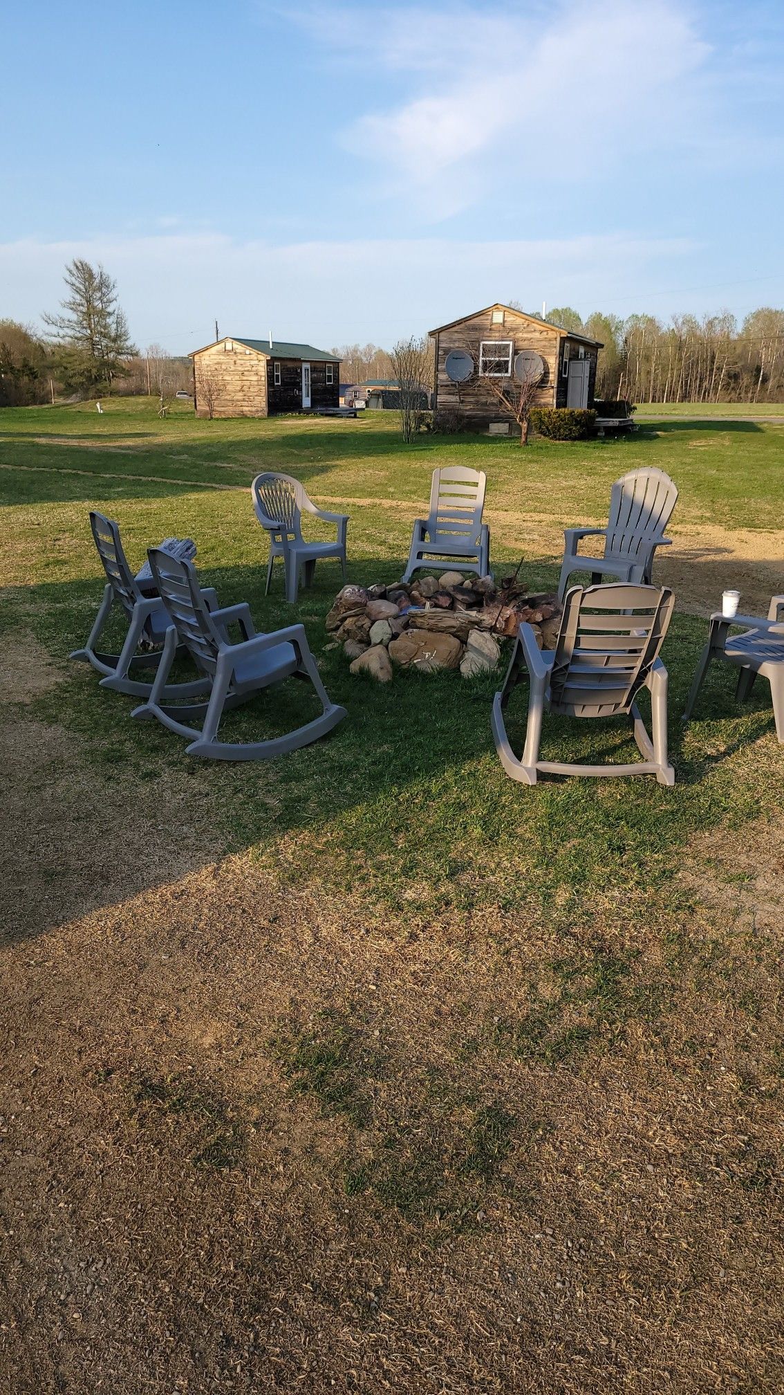 A group of rocking chairs are sitting around a fire pit in a grassy field.