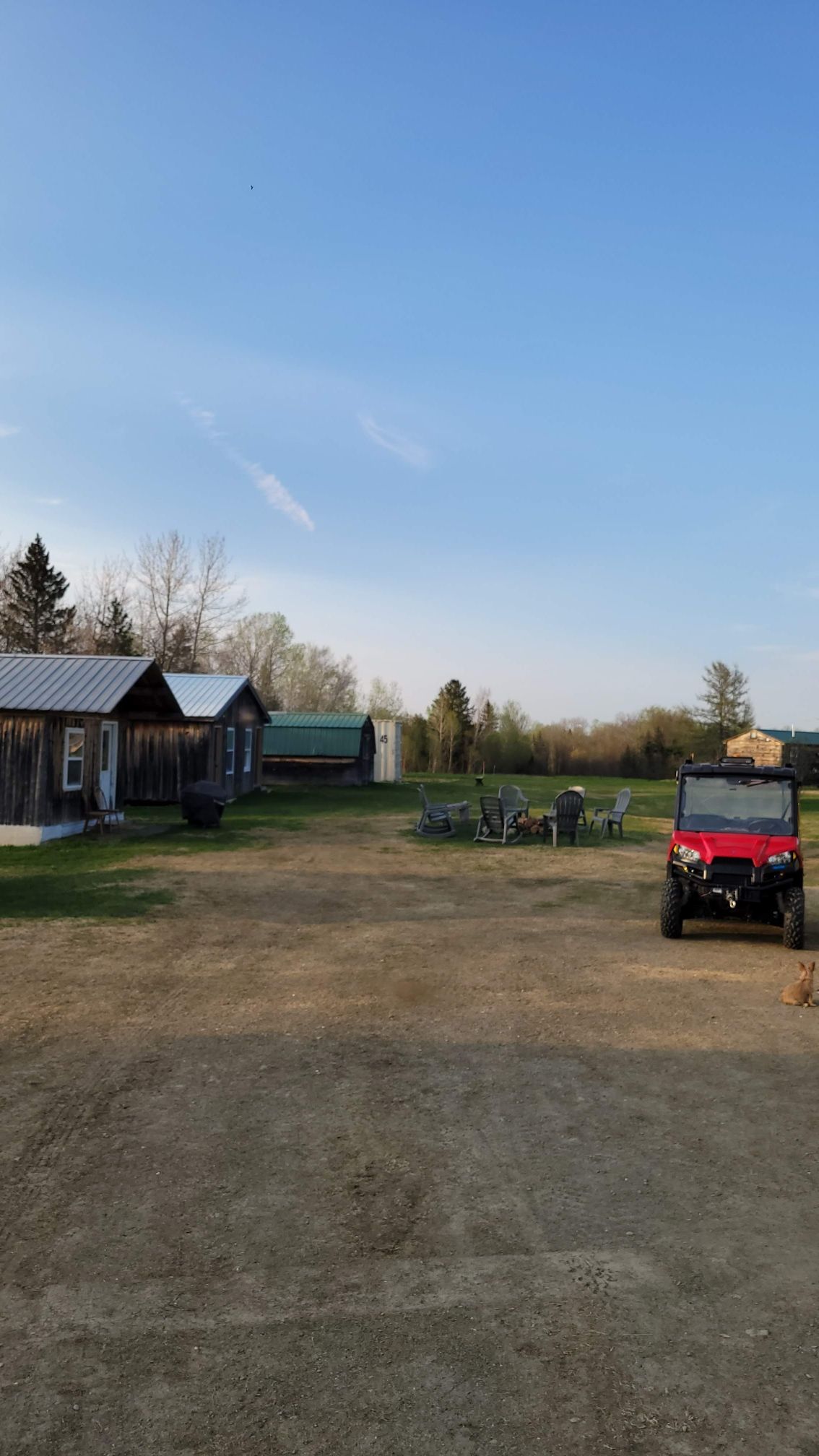 A red atv is parked in a dirt lot in front of a farm.