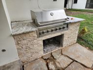 A stainless steel grill is built into a stone wall.