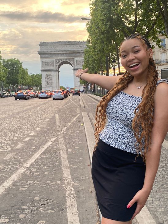 A woman is standing in front of a triumphal arch in paris.