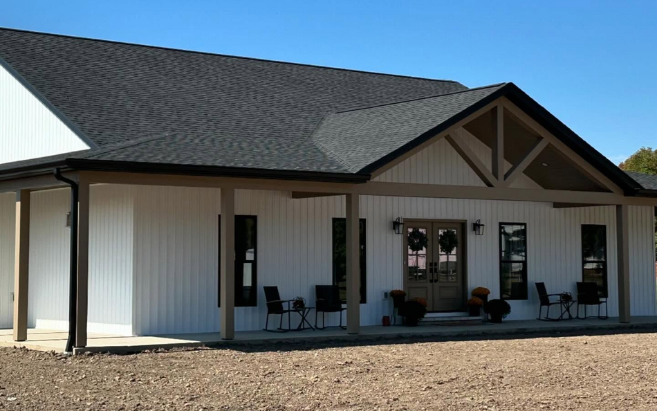 White building with black roof, porch, and double doors.
