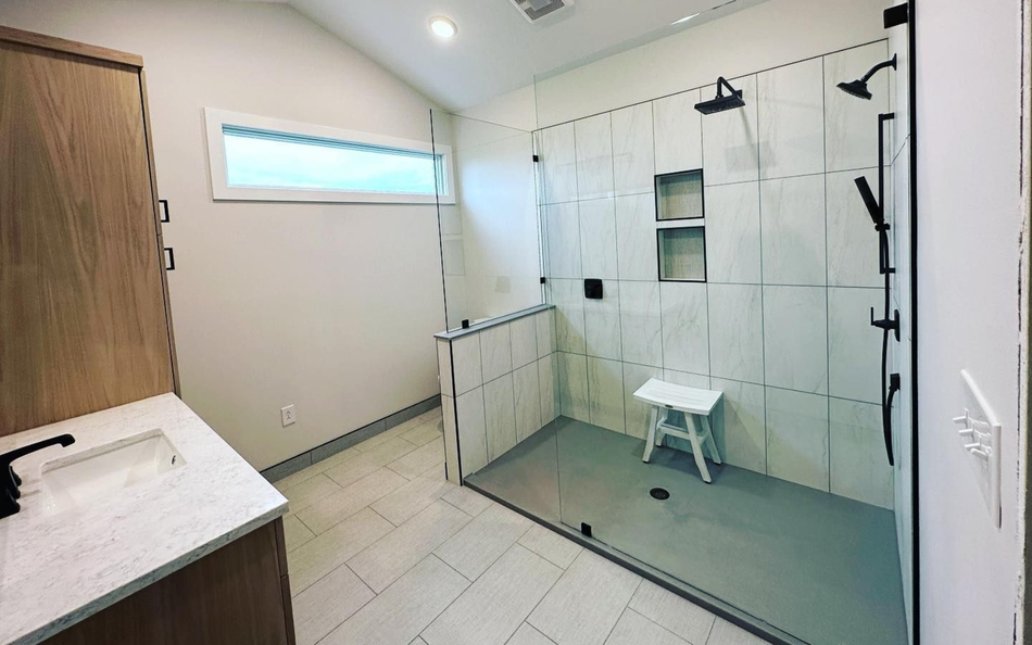 Modern bathroom with white tile shower, glass door, black fixtures, vanity, and cabinet.