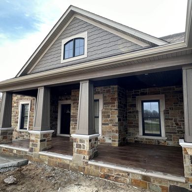 Stone house with a covered porch, gray and brown siding, dark trim, and windows.