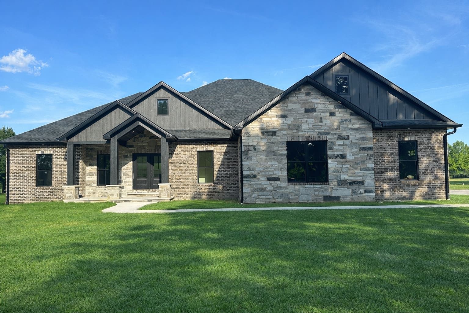 Stone house with a covered porch, gray and brown siding, dark trim, and windows.