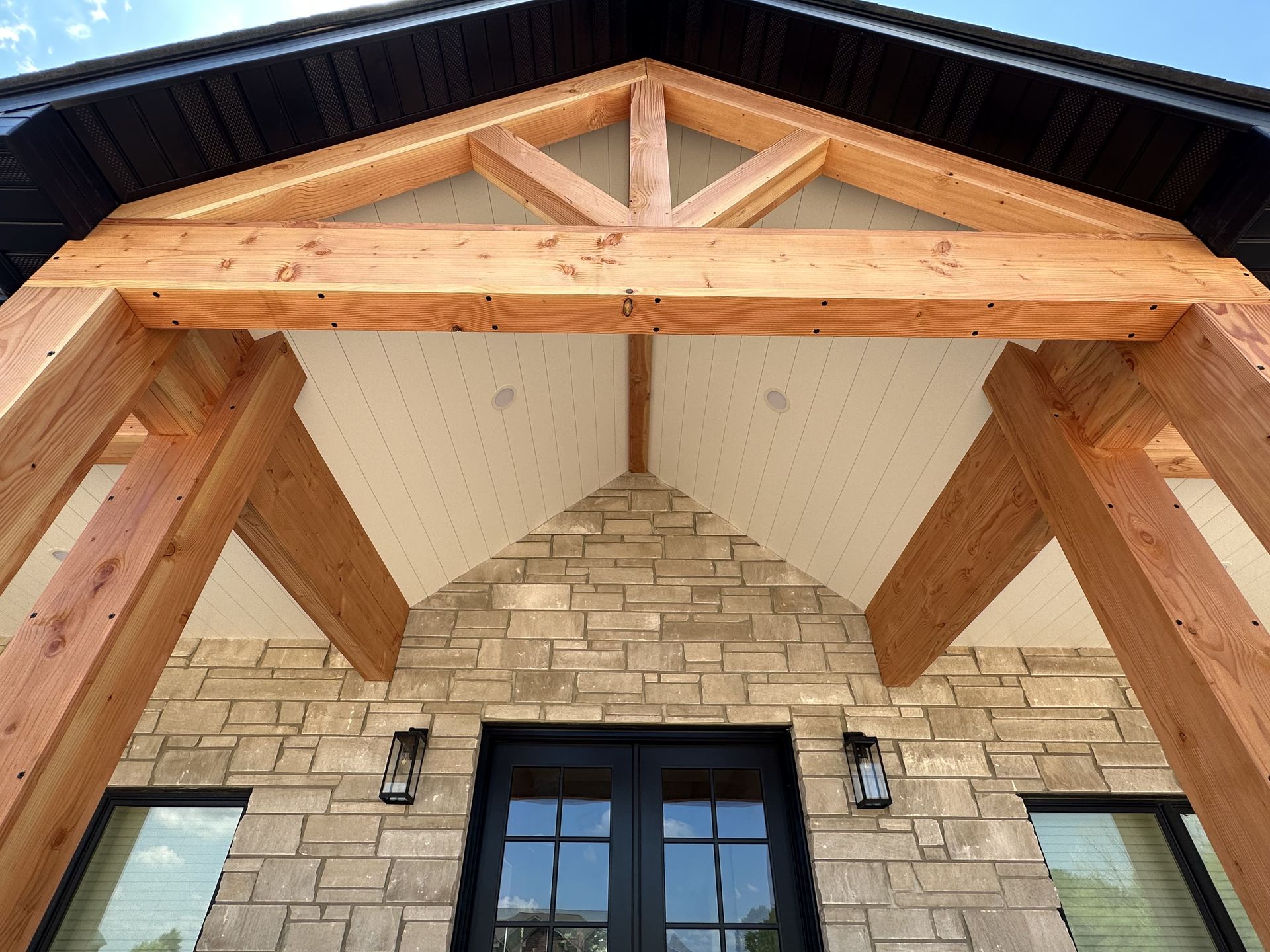 White building with black roof, porch, brown trim, double doors, and black chairs.