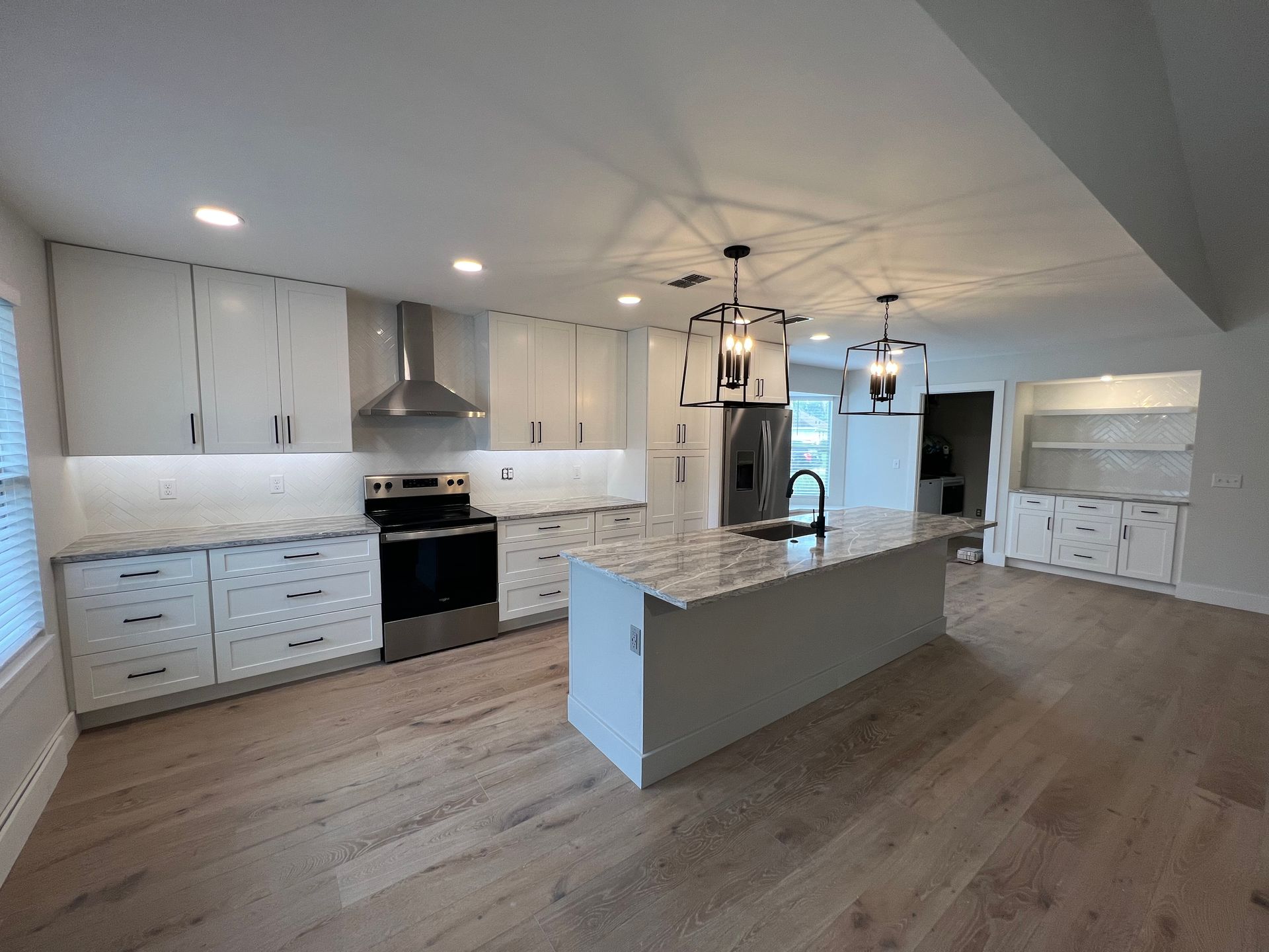 A kitchen with white cabinets , granite counter tops , stainless steel appliances and a large island.
