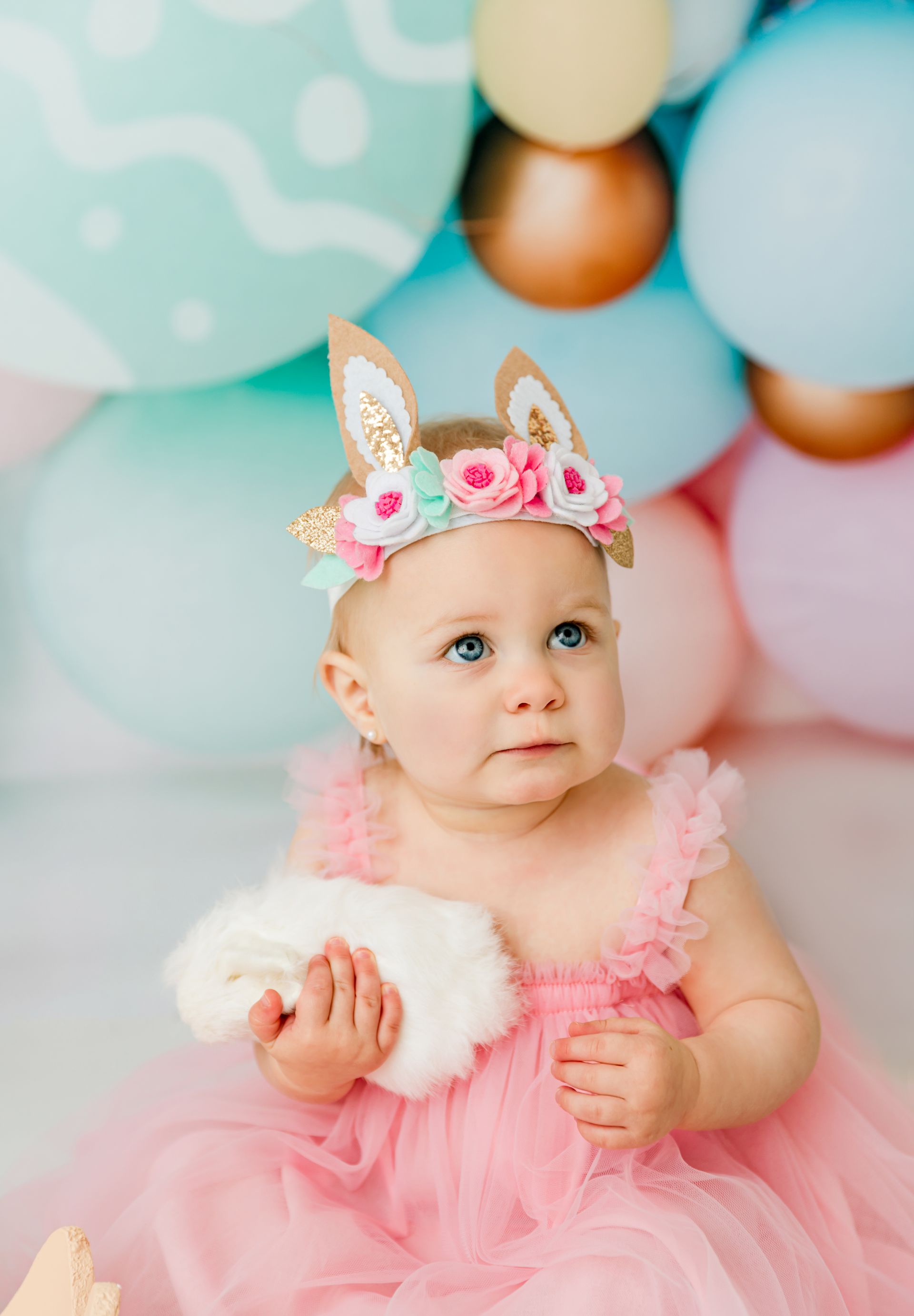 toddler girl in soft pink dress and bunny ears headband posing during Easter studio photography in Cary NC