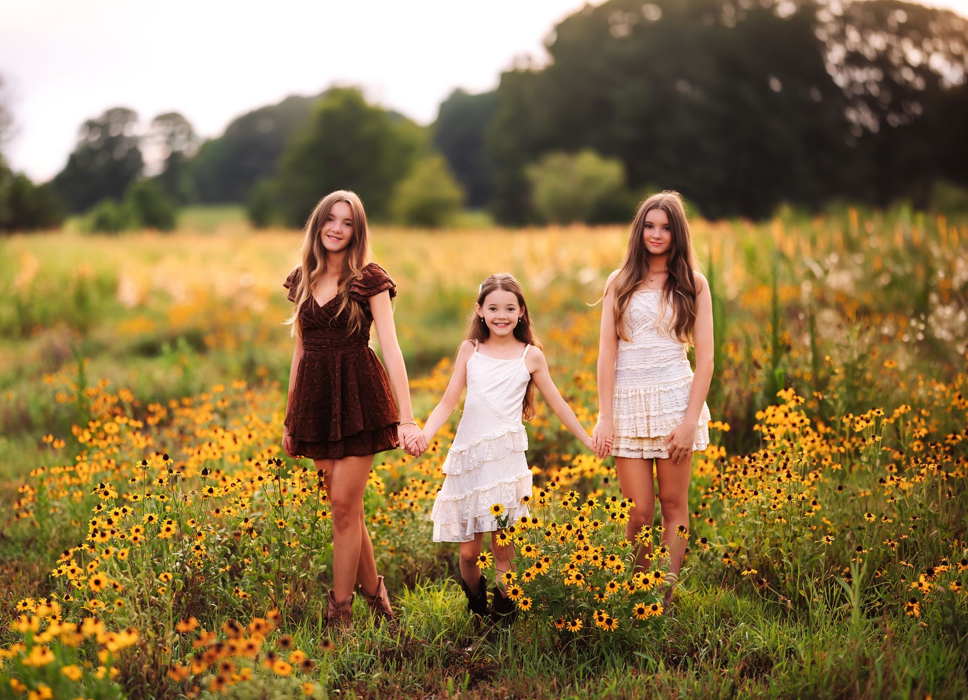Sisters walking hand in hand through a sunflower field at sunset.