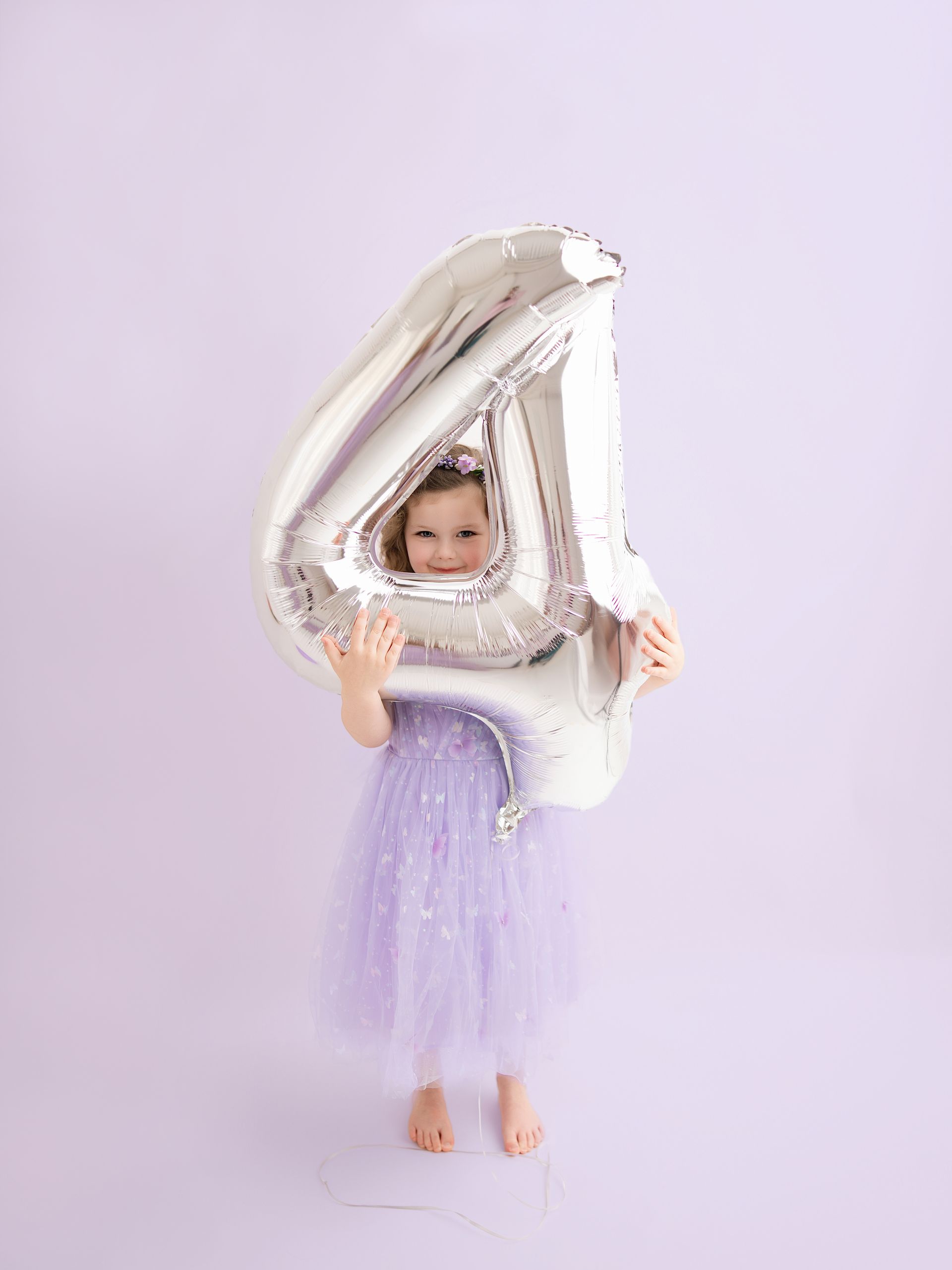 4-year-old girl holding a number 4 balloon during her birthday celebration photoshoot