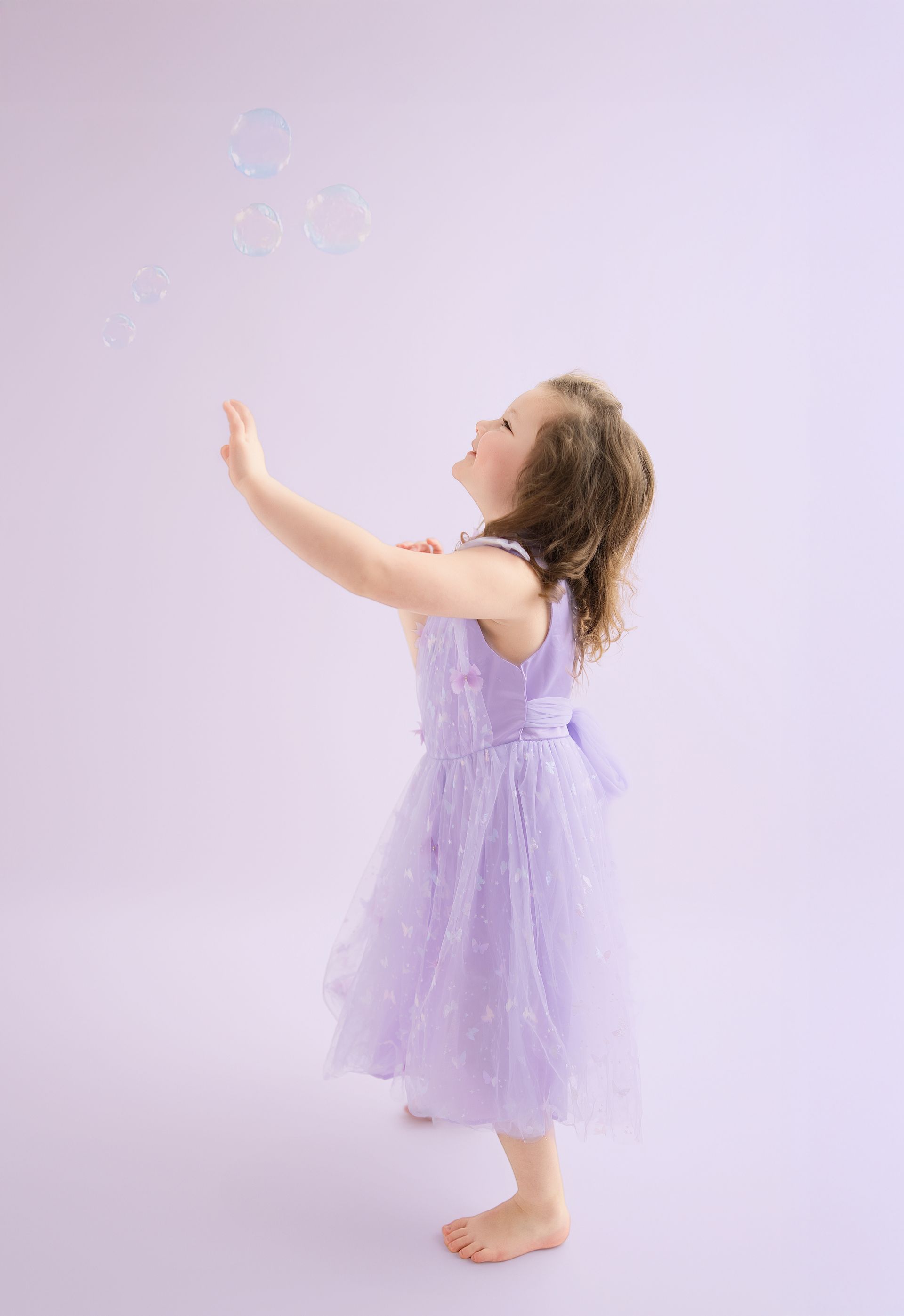 Little girl playing with bubbles during purple-themed mother-daughter photoshoot