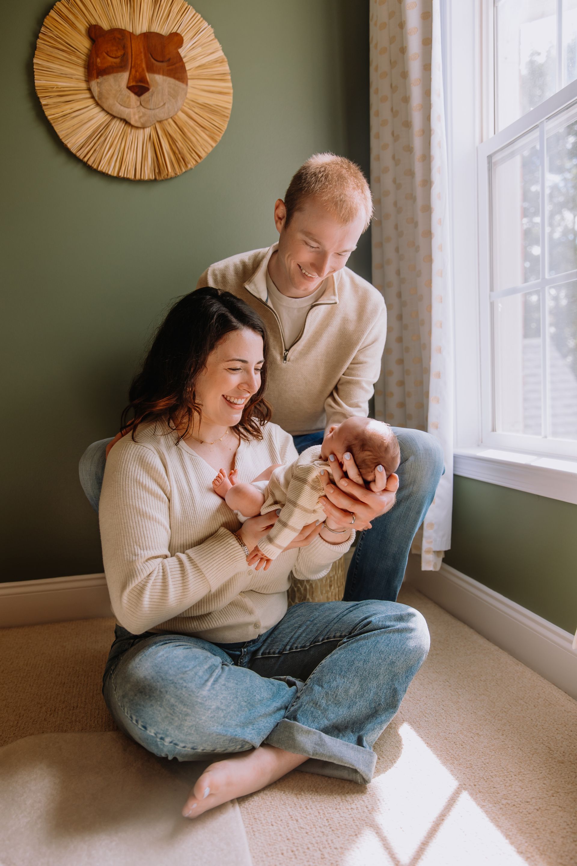 In-home newborn photography in Raleigh, NC. Parents holding the baby near the baby's nursery window