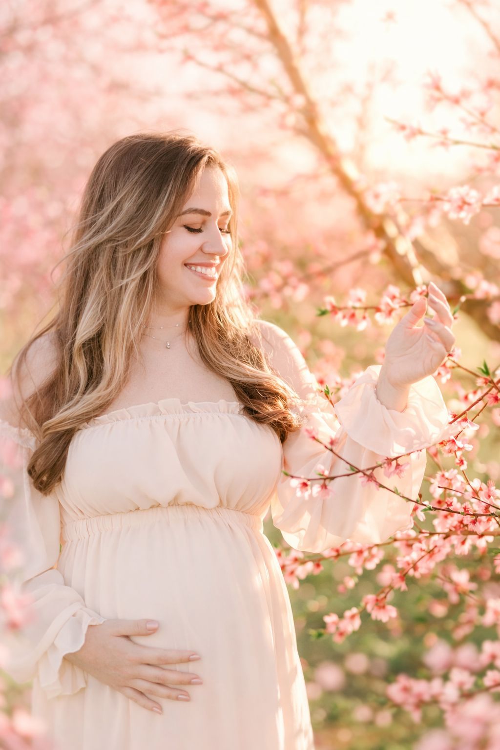 Expecting mother touching peach blossom branch during golden hour maternity session in Raleigh NC