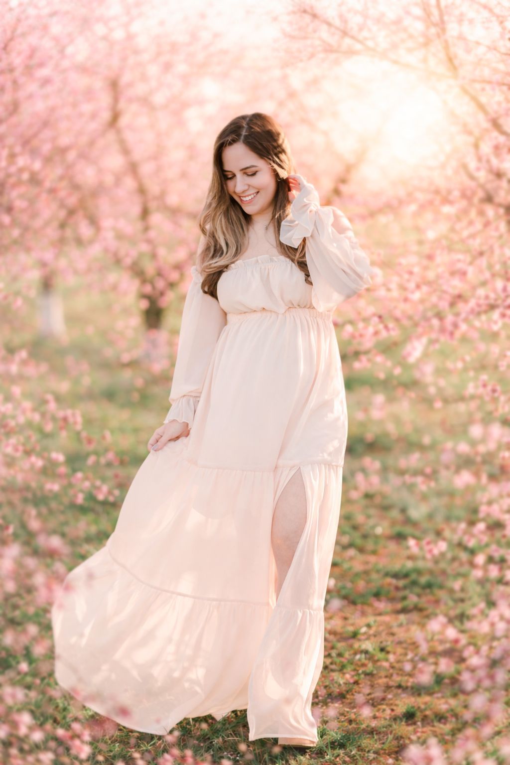 Pregnant woman walking through peach blossom orchard during spring maternity photography session in Raleigh NC