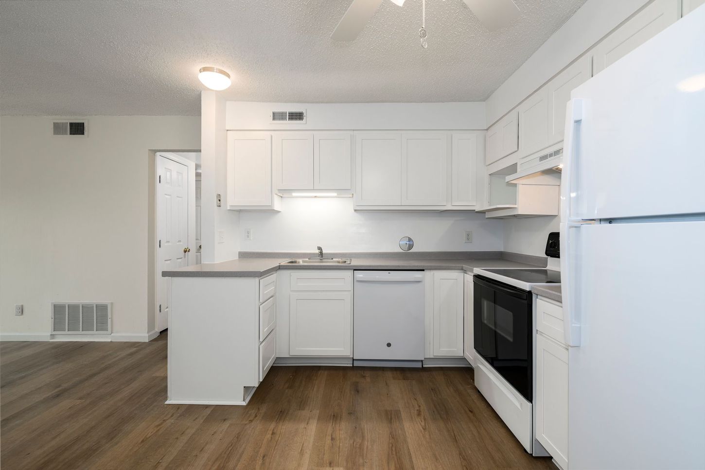 White kitchen with cabinets, appliances, and gray countertops. Wood-look flooring.