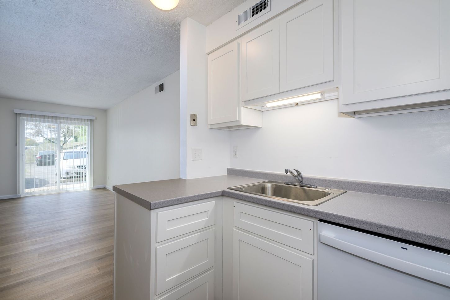 White kitchen with gray countertops, cabinets, and a sink. A sliding glass door leads to outside.