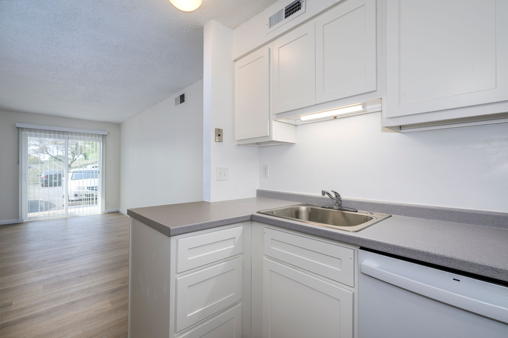 White kitchen with gray countertops, cabinets, and a sink. A sliding glass door leads to outside.