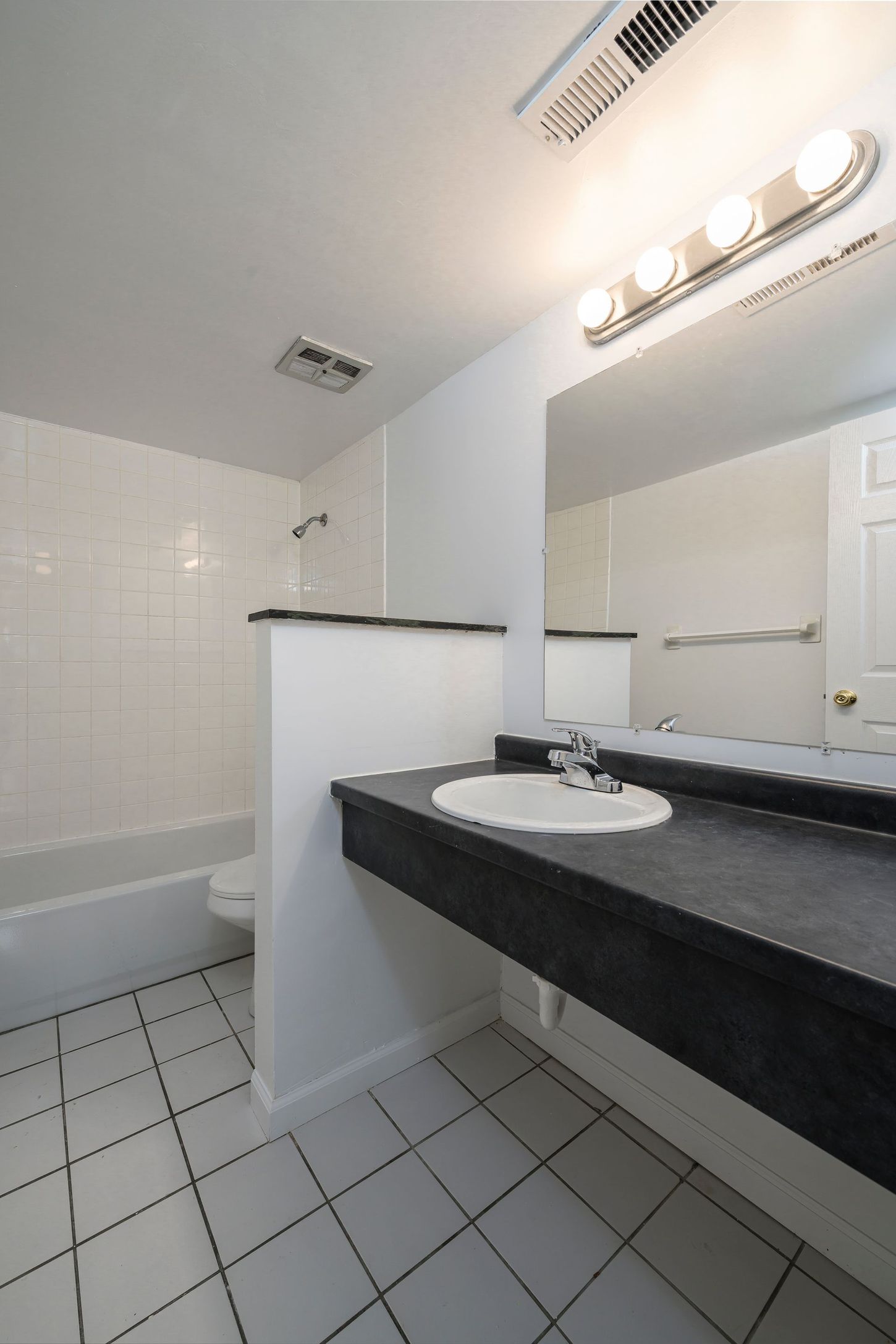Bathroom with white tile, dark countertop, and large mirror.
