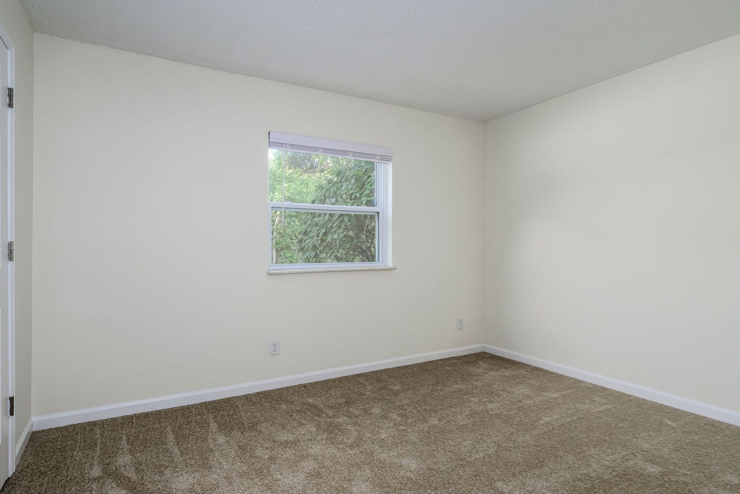 Empty room with beige walls, window, and brown carpet.