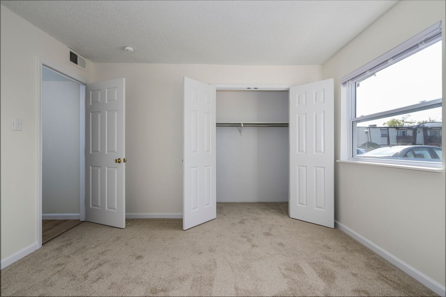 Empty bedroom with tan carpet, white walls, and a closet with open doors.