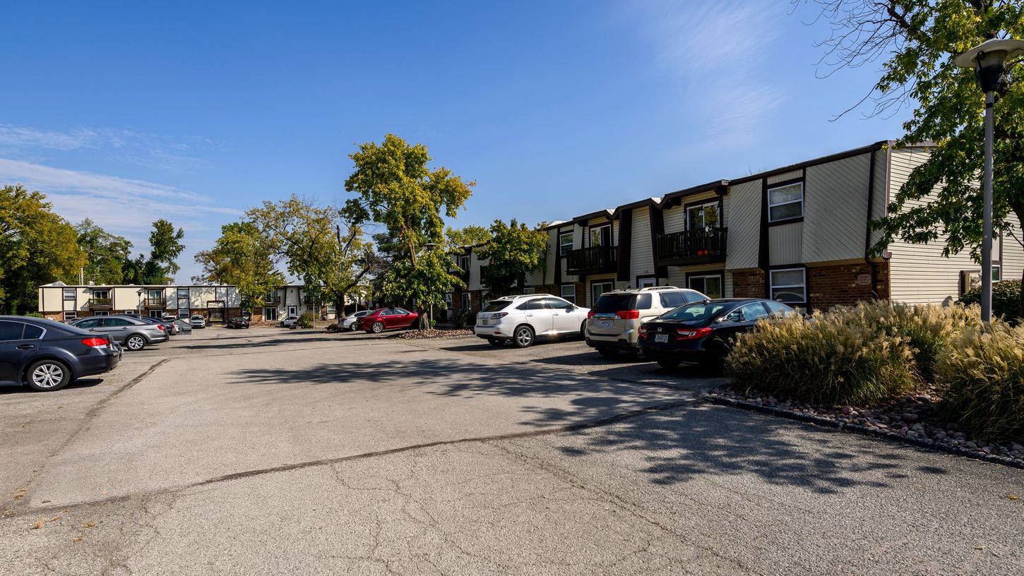 Parking lot with cars in front of two-story apartment buildings under a blue sky.