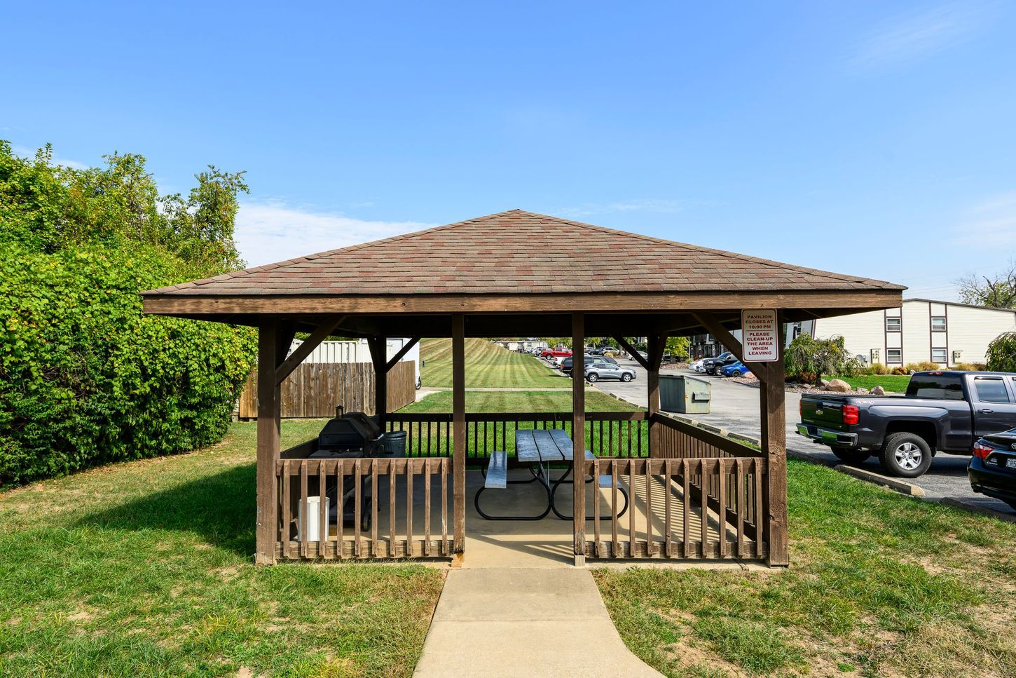 Gazebo with picnic table and grill on a grassy area, clear blue sky.