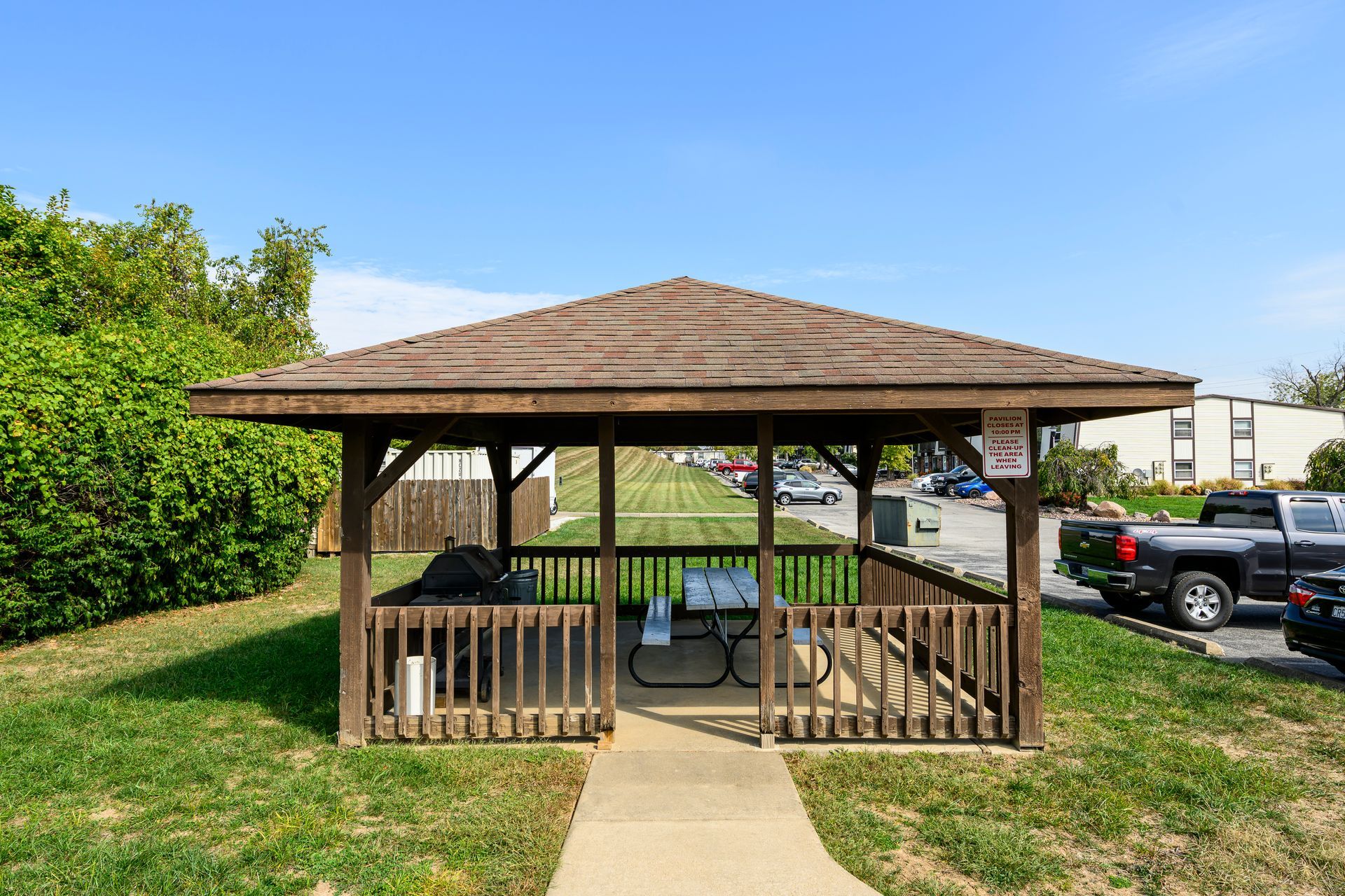 Gazebo with picnic table and grill on a grassy area, clear blue sky.