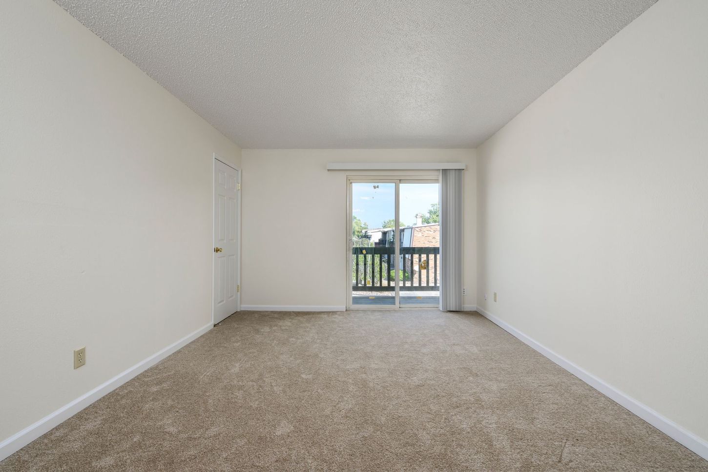 Empty room with carpet, sliding glass door leading to balcony, and a closed door.
