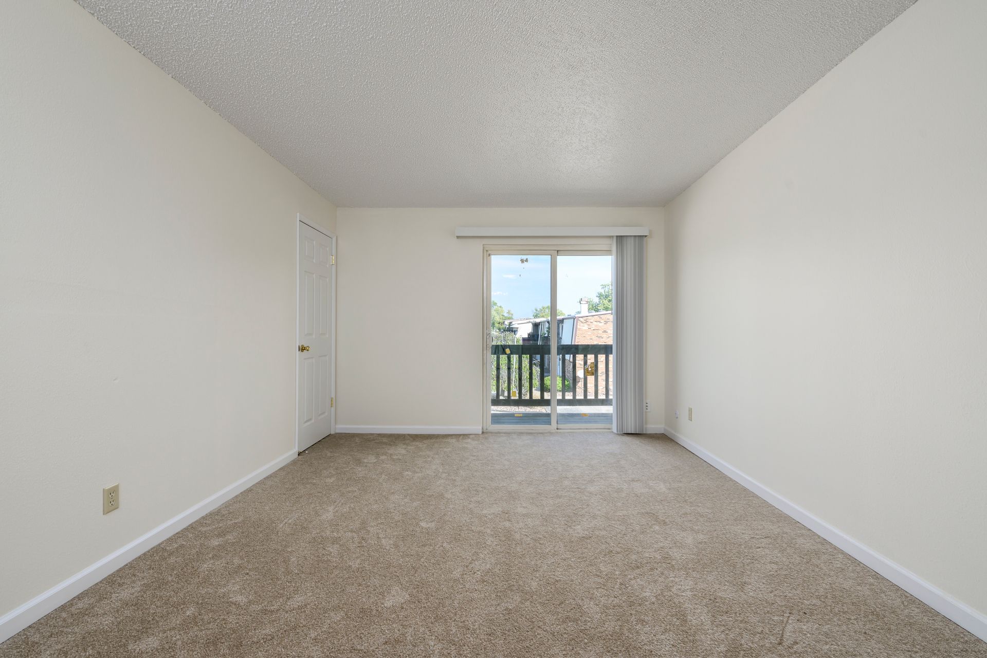 Empty room with carpet, sliding glass door leading to balcony, and a closed door.