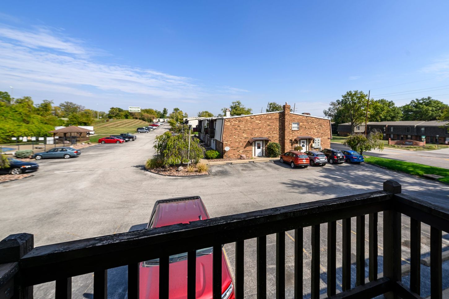 View from a balcony of a parking lot, brick building, cars, and trees on a sunny day.