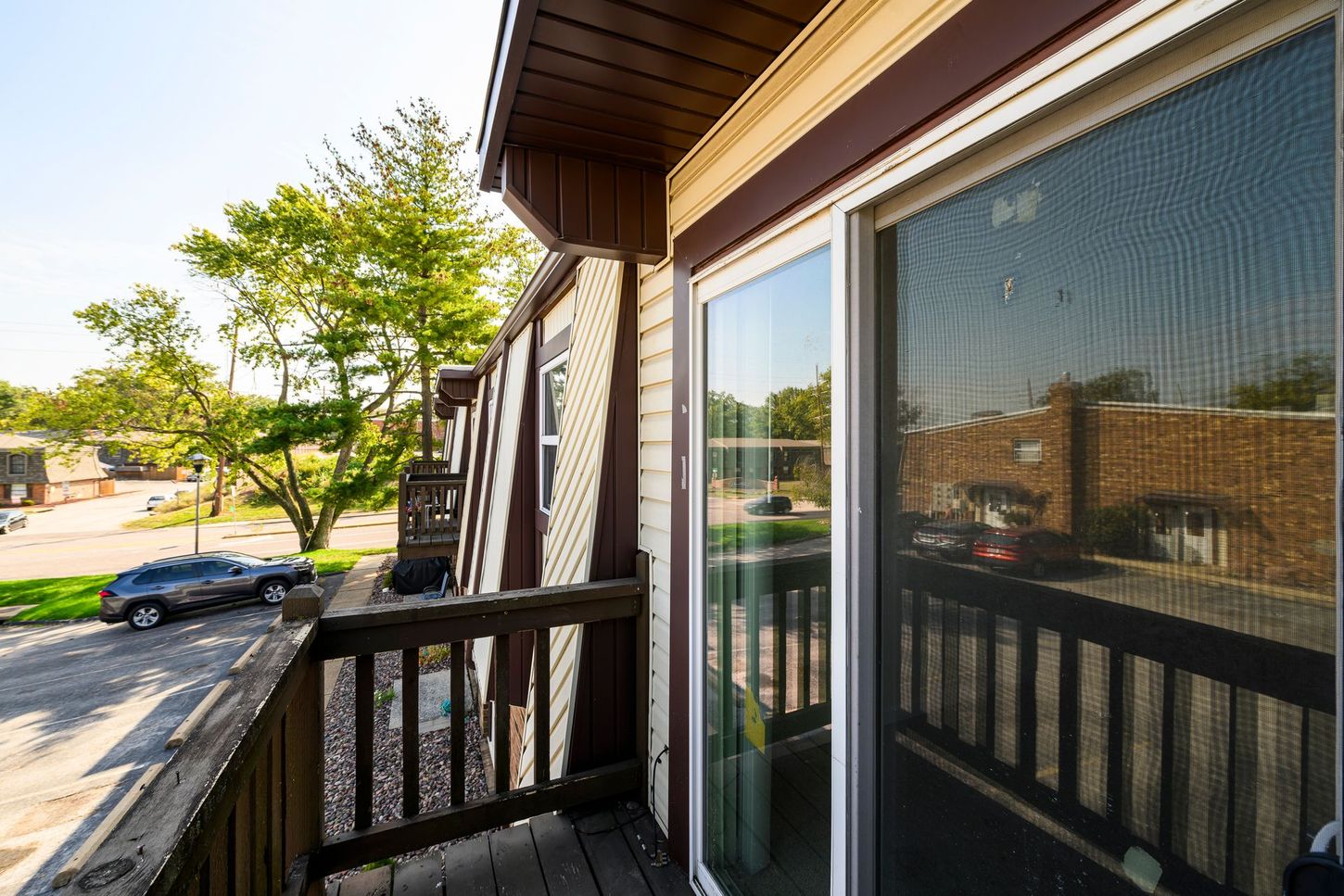 Balcony with a sliding glass door and a view of a street and buildings on a sunny day.