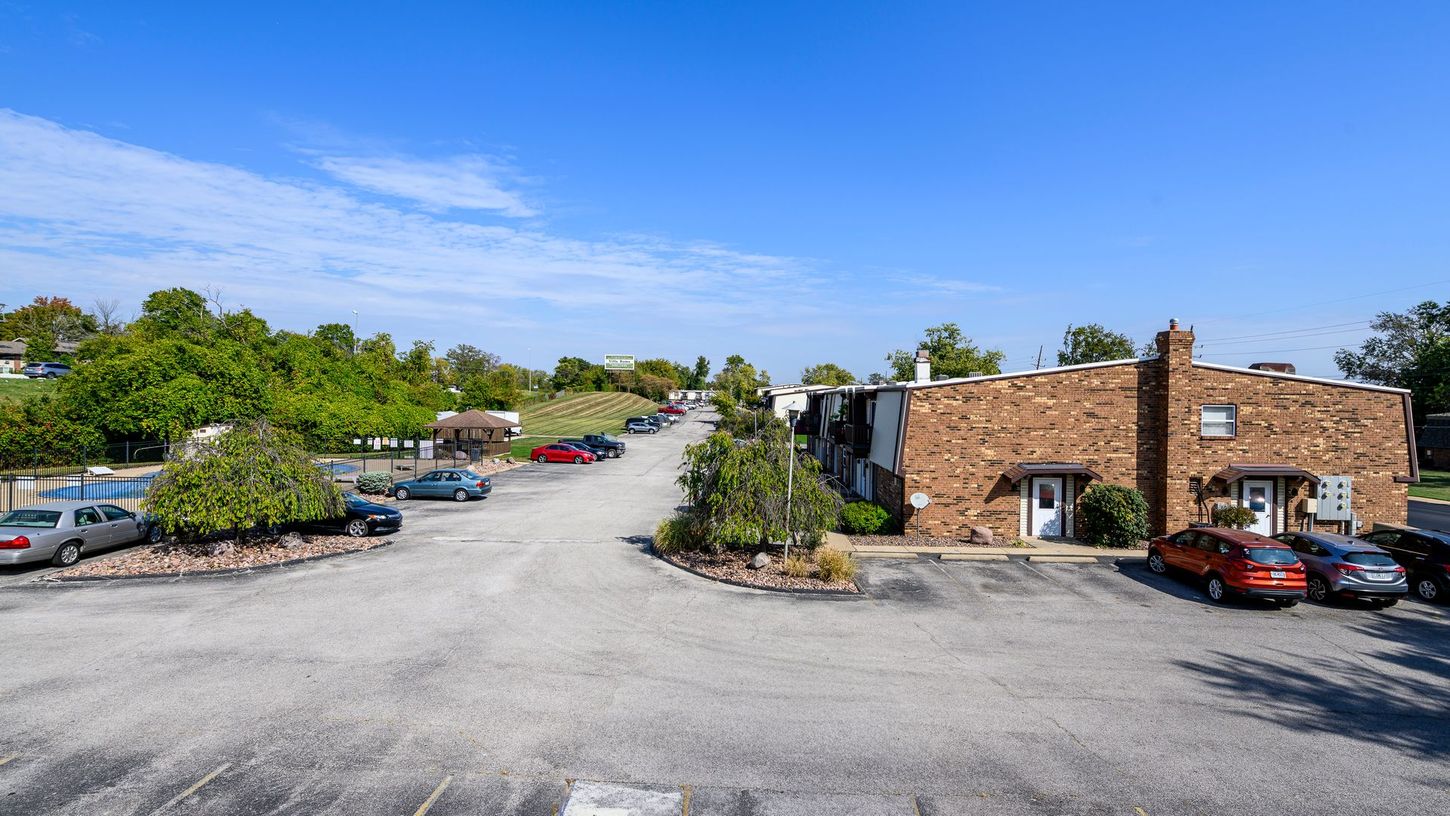 Parking lot in front of a brick building and rows of parked cars under a blue sky.