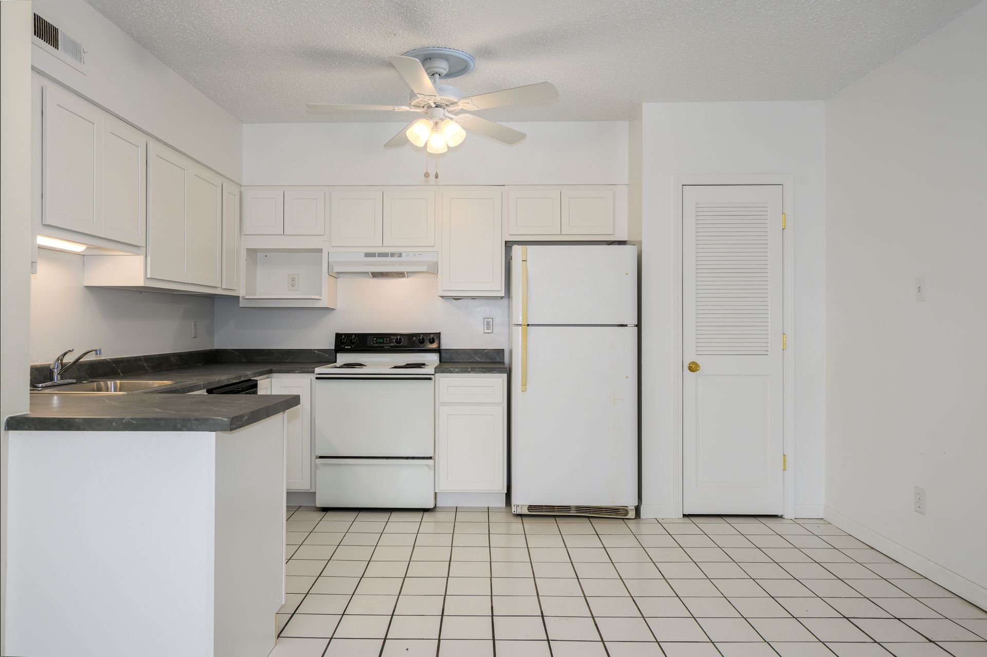 White kitchen with cabinets, appliances, and tile floor. Includes a refrigerator, stove, and a small counter.