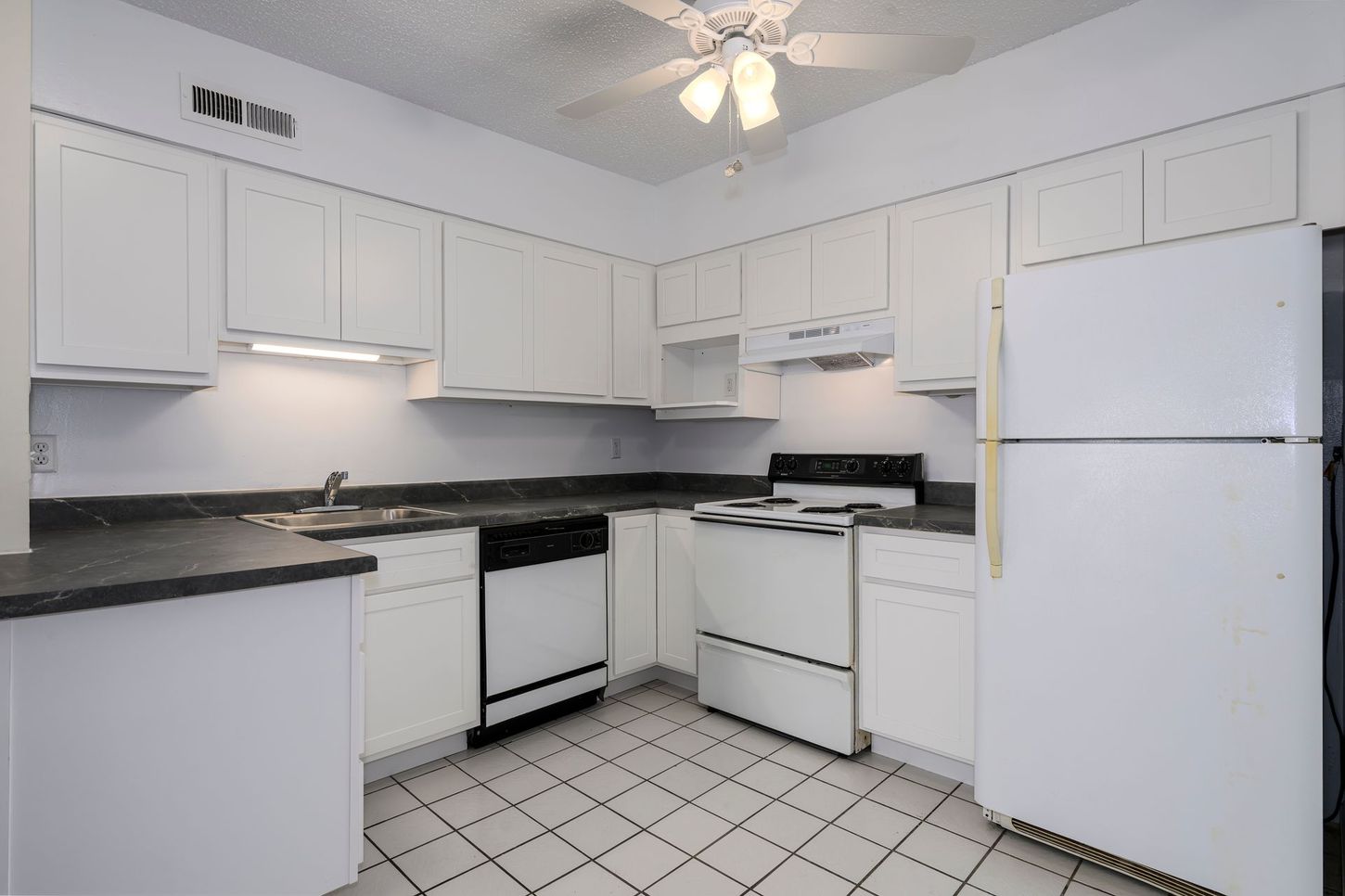 White kitchen with black countertops, appliances, cabinets, and a tiled floor.