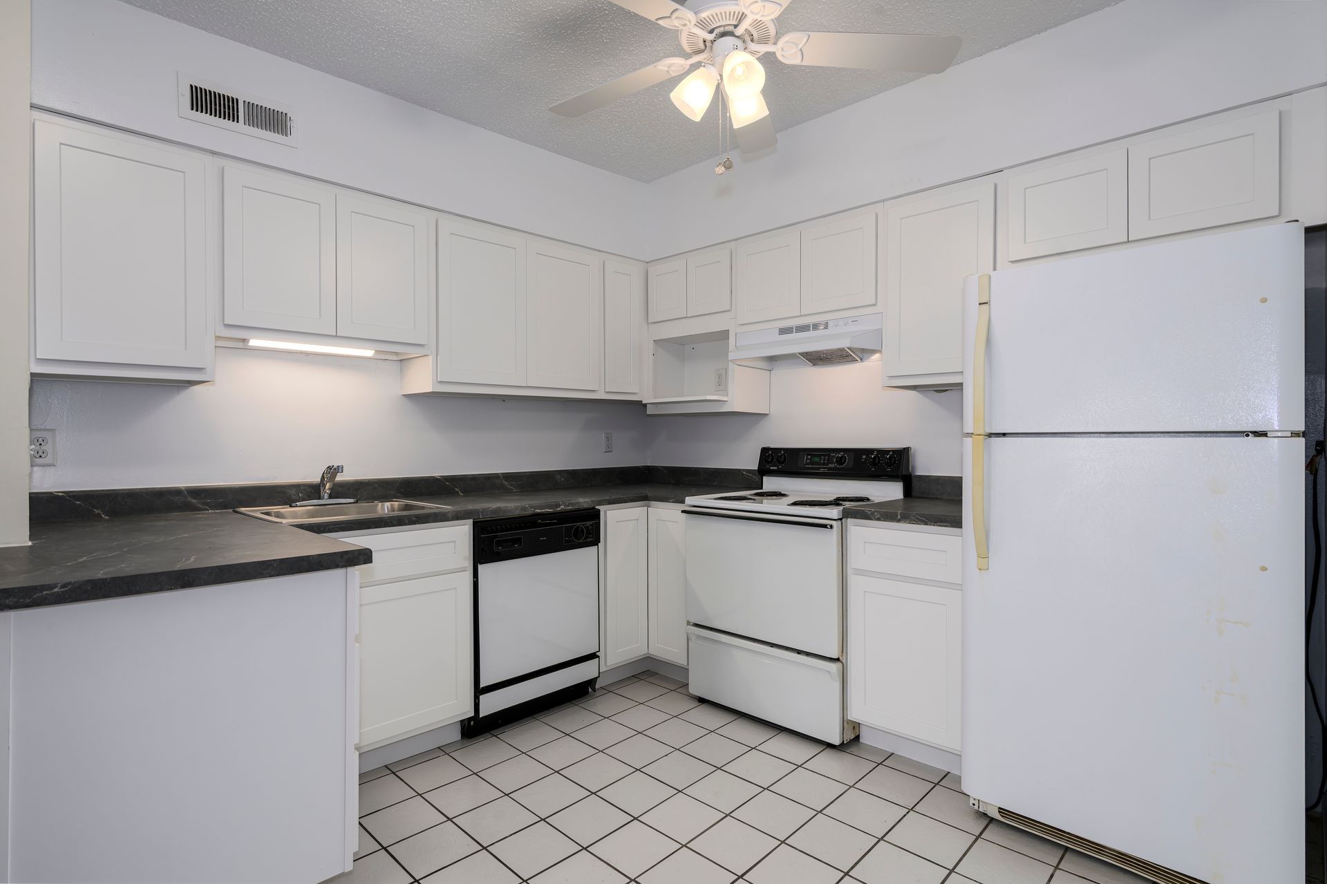 White kitchen with black countertops, appliances, cabinets, and a tiled floor.