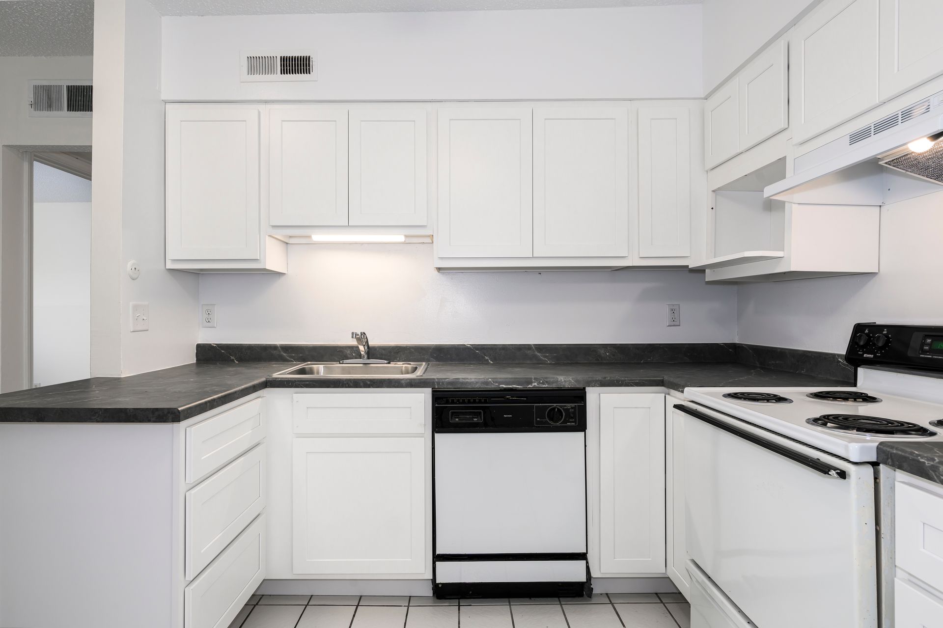 White kitchen with white cabinets, black countertops, and black appliances.