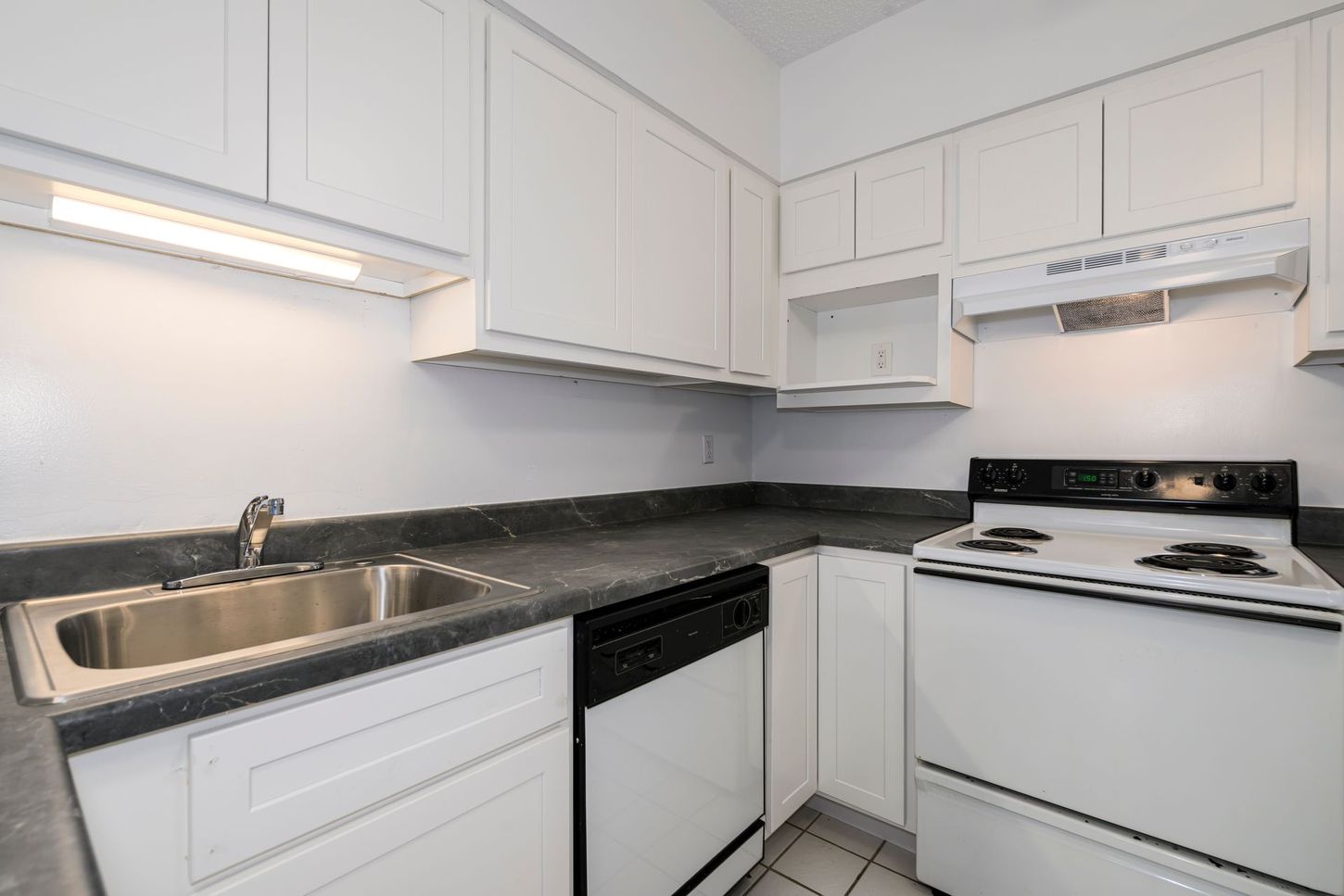 White kitchen with dark countertops, stainless steel sink, and white appliances.