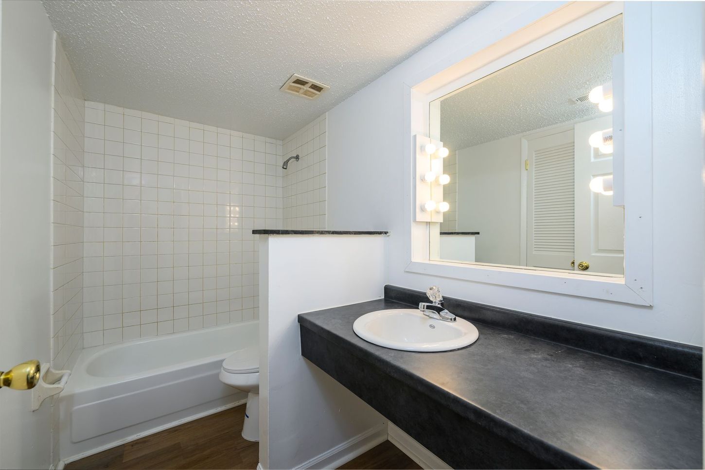 Bathroom with white tile, a bathtub, a sink, and a large mirror.