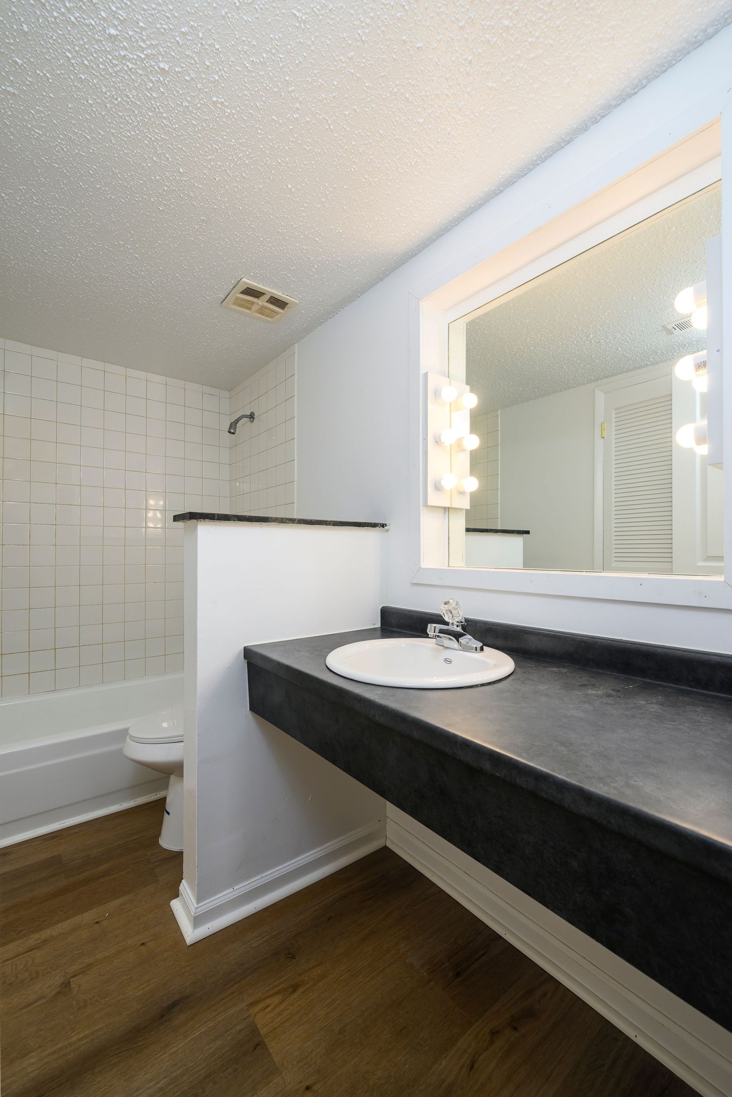 Bathroom with a white wall, black countertop with sink, and a large mirror with lights.