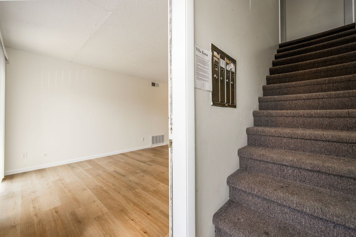 Interior: empty room with wood floor visible through doorway, stairs with carpet on right.