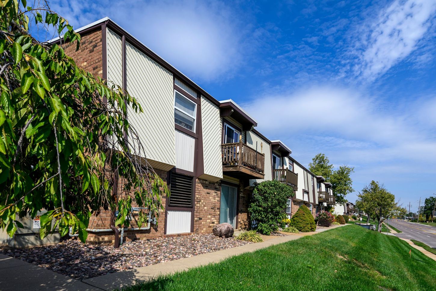 Apartment building with brick and white siding, balconies, and green grass under a blue sky.