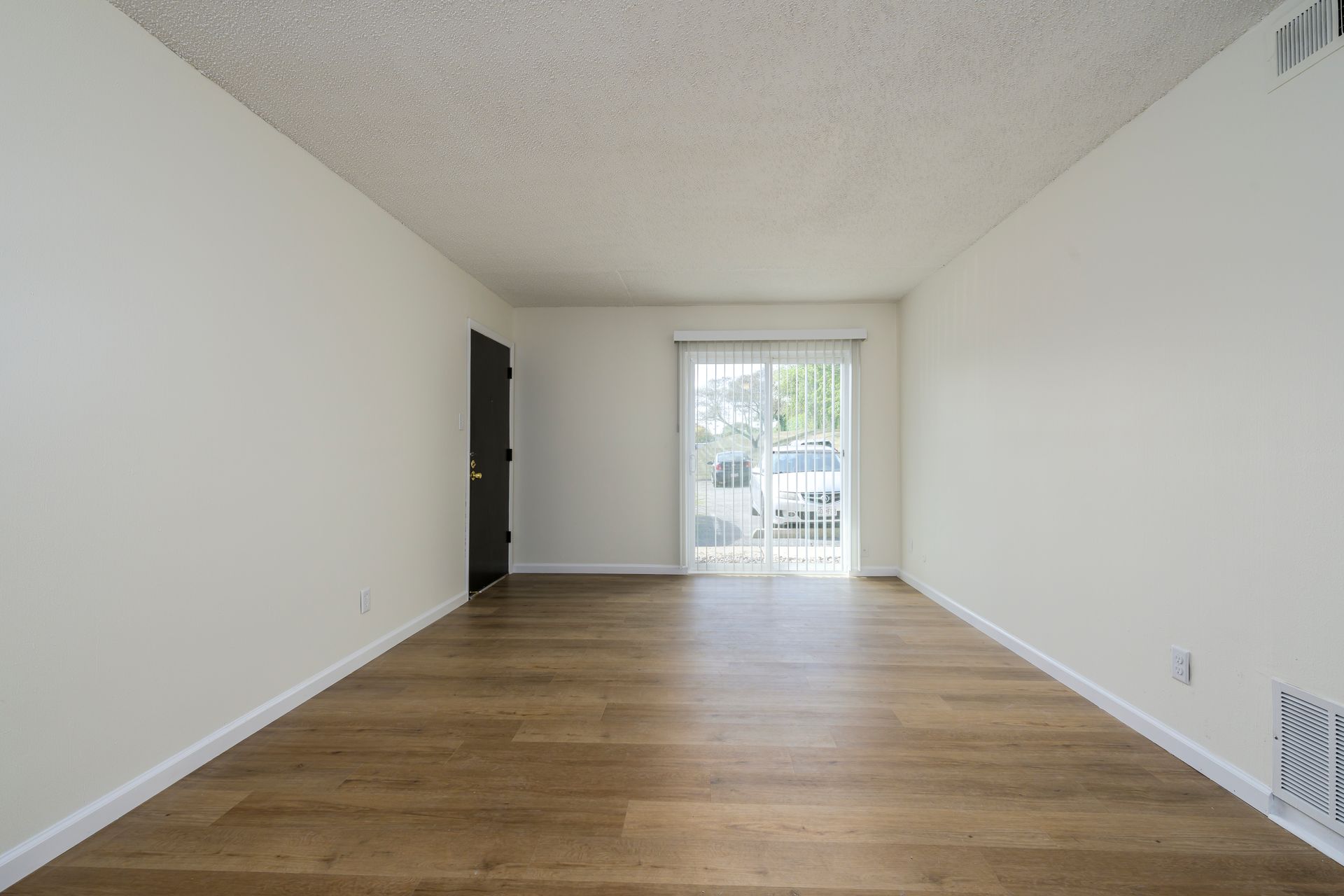 Empty room with wood-look floor, sliding glass door, white walls, and a black door.