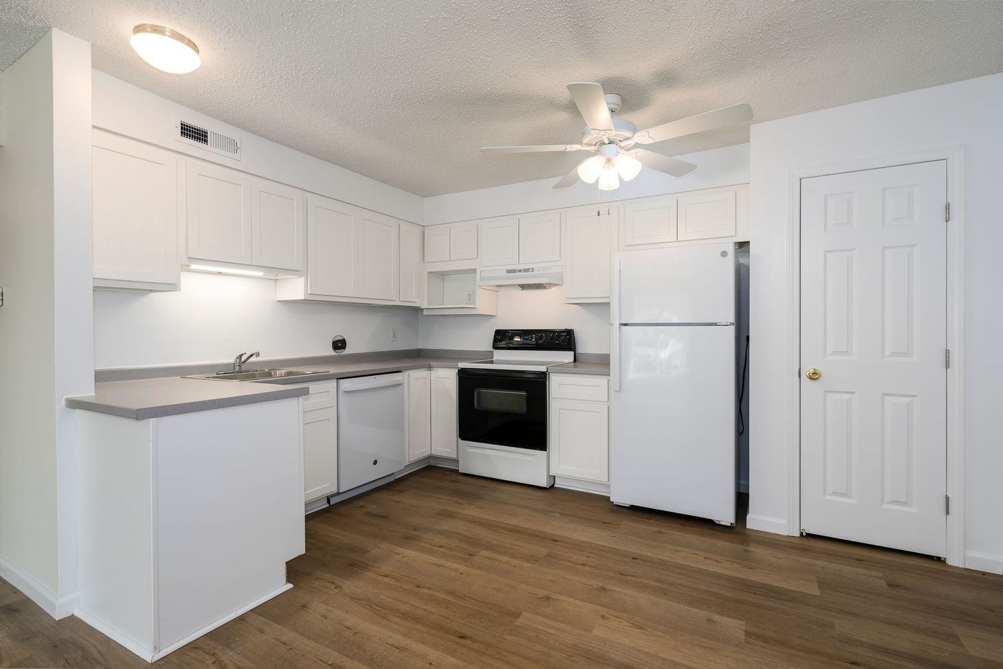 White kitchen with cabinets, appliances, and wooden flooring.