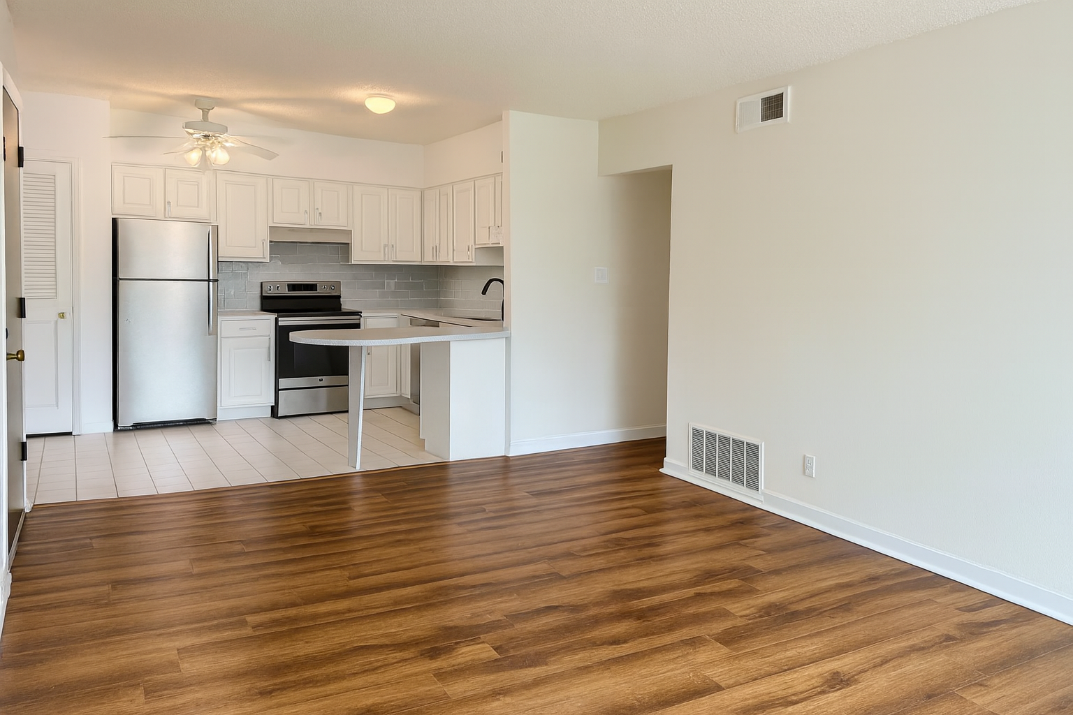 Bright, open-plan kitchen and living area with white cabinets and walls, stainless steel appliances, and wood floors.