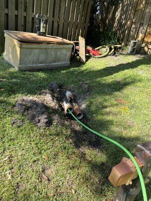 A green hose is connected to a wooden box in a backyard.