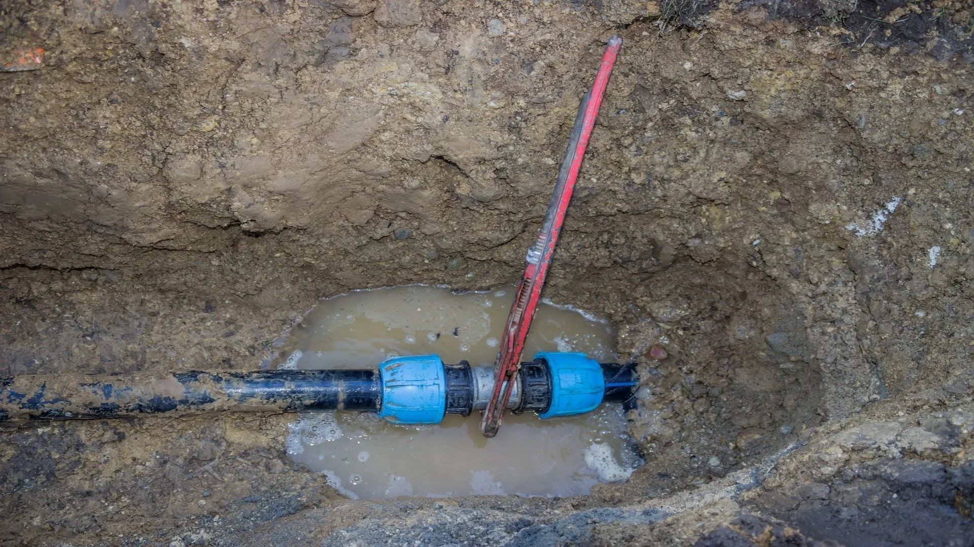 A broken water pipe is sitting in the dirt in a hole.