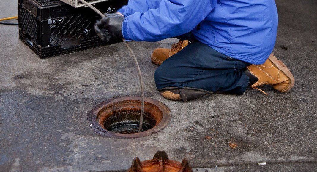 A man is cleaning a toilet with a hose.