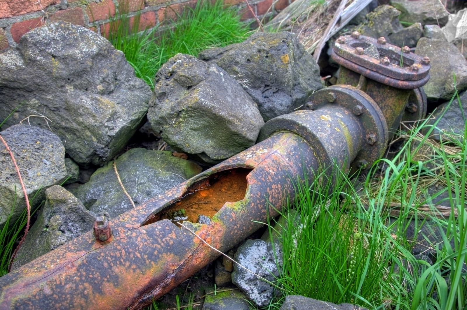 A rusty pipe with a hole in it is sitting on top of a pile of rocks.
