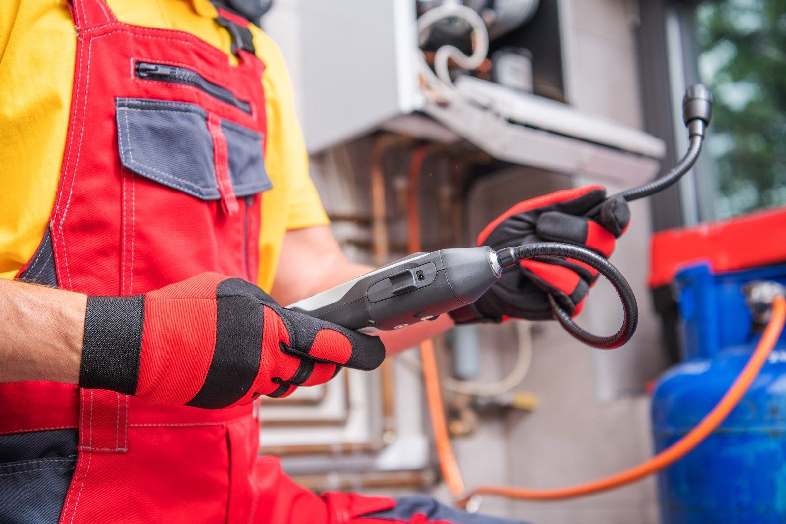A man in red and yellow overalls is holding a hose and a tool.