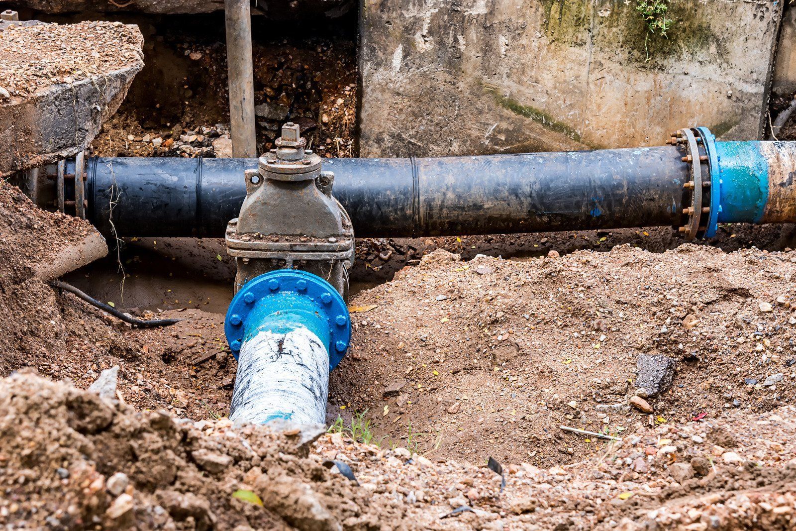 A water pipe is sitting in the dirt next to a wall.