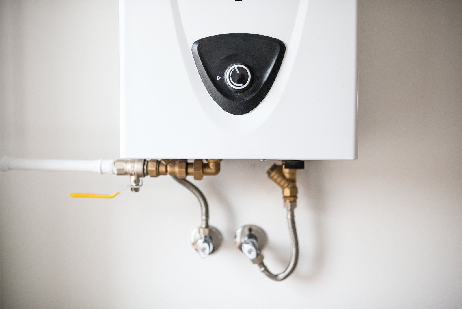 A close up of a water heater hanging on a wall.